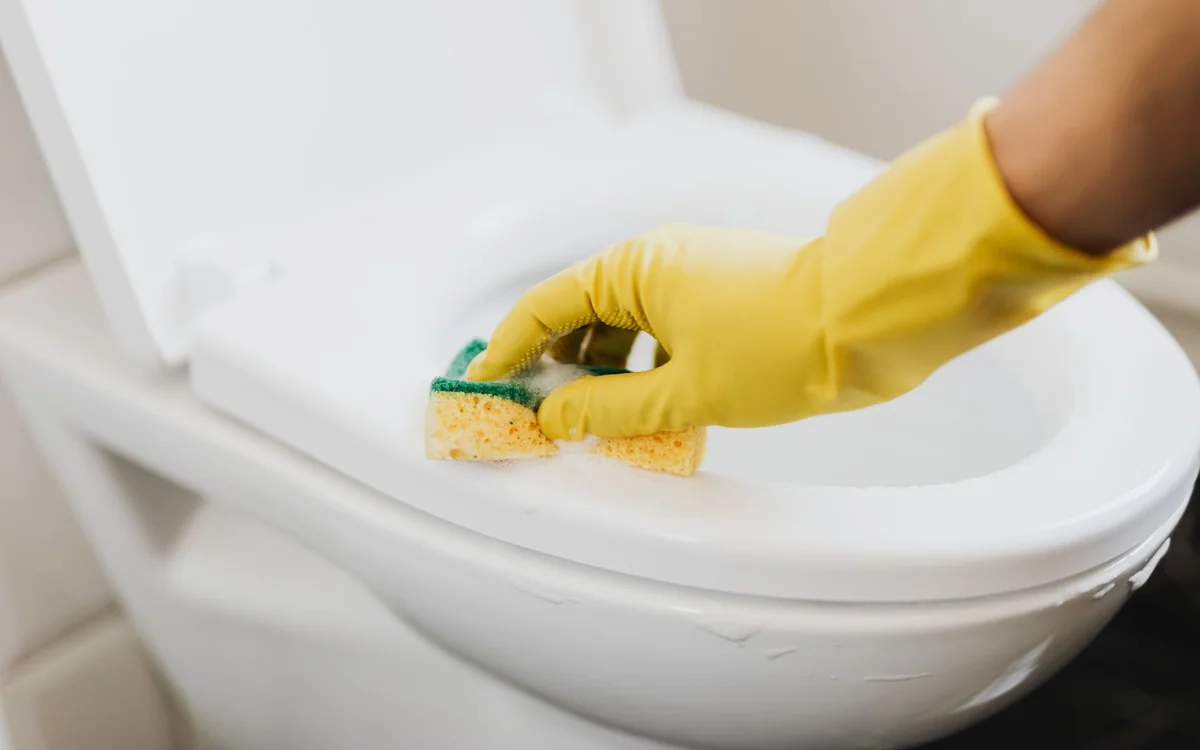 A wet bathroom floor mat being lifted for cleaning beside a bathtub